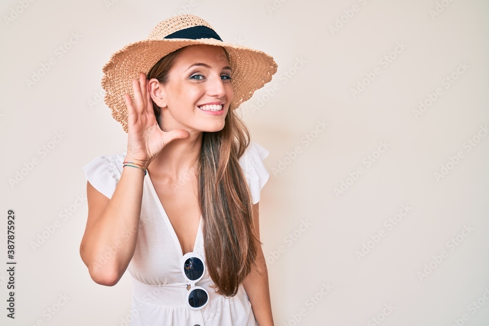 Young blonde girl wearing summer hat smiling with hand over ear listening and hearing to rumor or gossip. deafness concept. Young blonde girl wearing summer hat smiling with hand over ear listening and hearing to rumor or gossip. deafness concept.
