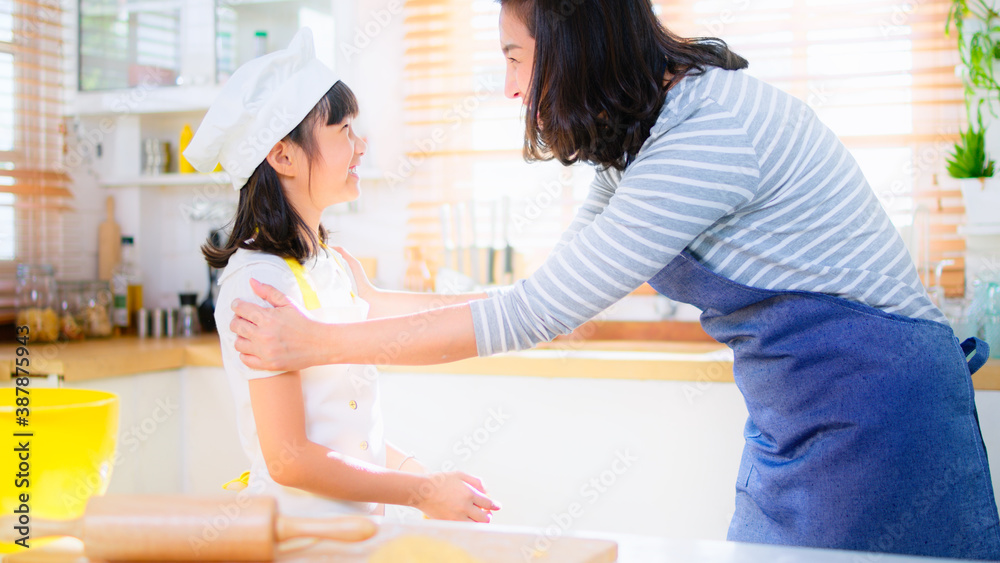 Young Asian mother help daughter wear apron and chef hat, prepare to learn bake pastry in kitchen at home. family love relationship, smart kid's growth, home cooking, or food making concept. Young Asian mother help daughter wear apron and chef hat, prepare to learn bake pastry in kitchen at home. family love relationship, smart kid's growth, home cooking, or food making concept.