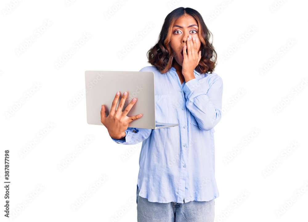Young beautiful mixed race woman working using computer laptop covering mouth with hand, shocked and afraid for mistake. surprised expression Young beautiful mixed race woman working using computer laptop covering mouth with hand, shocked and afraid for mistake. surprised expression