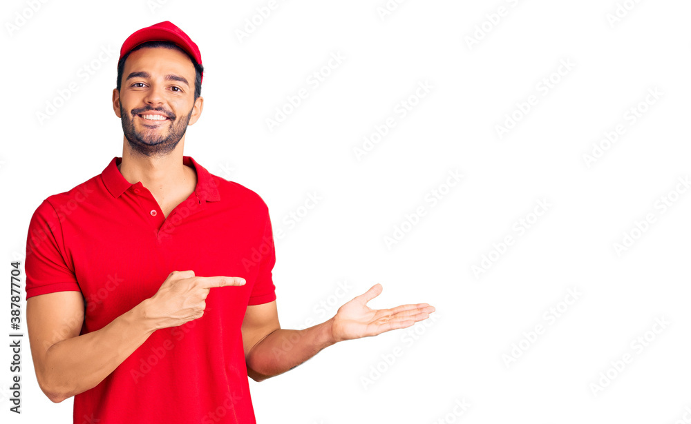 Young handsome hispanic man wearing delivery courier uniform amazed and smiling to the camera while presenting with hand and pointing with finger. Young handsome hispanic man wearing delivery courier uniform amazed and smiling to the camera while presenting with hand and pointing with finger.