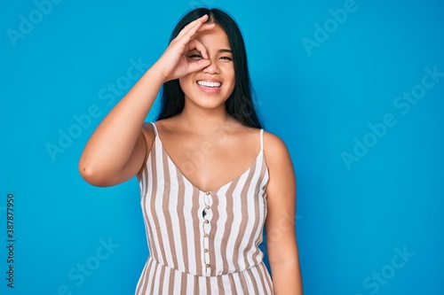 Young beautiful asian girl wearing casual clothes doing ok gesture with hand smiling, eye looking through fingers with happy face.
