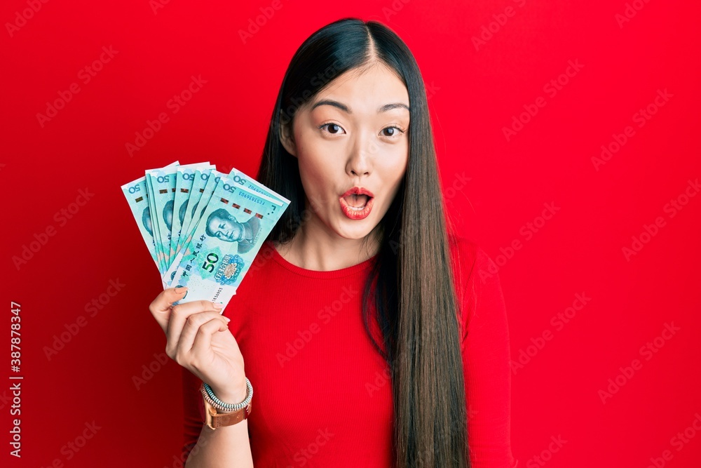 Young chinese woman holding 50 yuan chinese banknotes scared and amazed with open mouth for surprise, disbelief face Young chinese woman holding 50 yuan chinese banknotes scared and amazed with open mouth for surprise, disbelief face