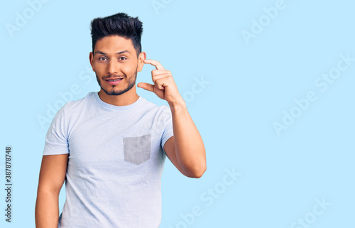 Handsome latin american young man wearing casual clothes smiling and confident gesturing with hand doing small size sign with fingers looking and the camera. measure concept.