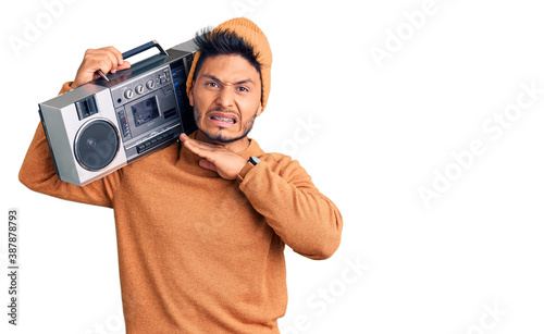Handsome latin american young man holding boombox, listening to music cutting throat with hand as knife, threaten aggression with furious violence