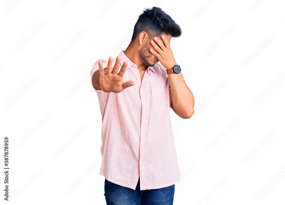 Handsome latin american young man wearing casual summer shirt covering eyes with hands and doing stop gesture with sad and fear expression. embarrassed and negative concept. Handsome latin american young man wearing casual summer shirt covering eyes with hands and doing stop gesture with sad and fear expression. embarrassed and negative concept.