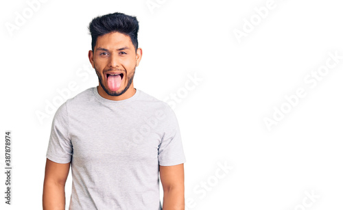 Handsome latin american young man wearing casual tshirt sticking tongue out happy with funny expression. emotion concept.