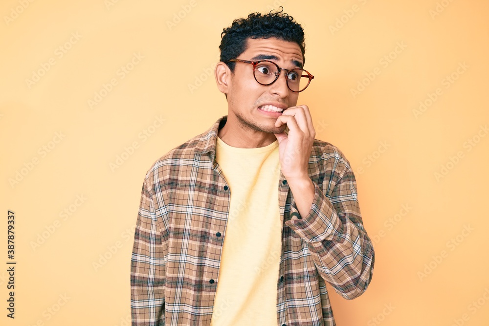 Young handsome hispanic man wearing casual clothes and glasses looking stressed and nervous with hands on mouth biting nails. anxiety problem. Young handsome hispanic man wearing casual clothes and glasses looking stressed and nervous with hands on mouth biting nails. anxiety problem.