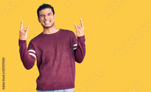 Hispanic handsome young man wearing casual clothes shouting with crazy expression doing rock symbol with hands up. music star. heavy concept.