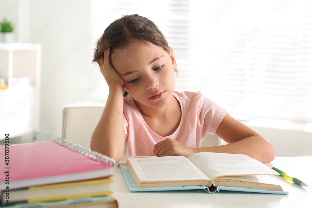Sad little girl doing homework at table indoors Sad little girl doing homework at table indoors