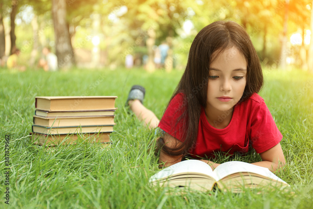 Cute little girl reading book on green grass in park Cute little girl reading book on green grass in park