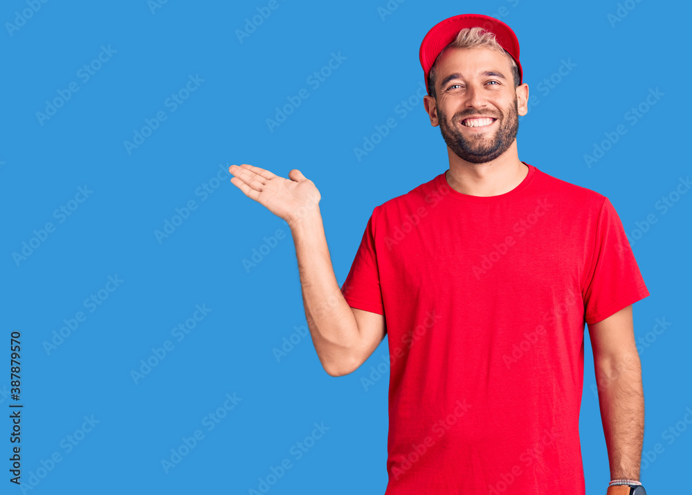 Young handsome blond man wearing t-shirt and cap smiling cheerful presenting and pointing with palm of hand looking at the camera. Young handsome blond man wearing t-shirt and cap smiling cheerful presenting and pointing with palm of hand looking at the camera.