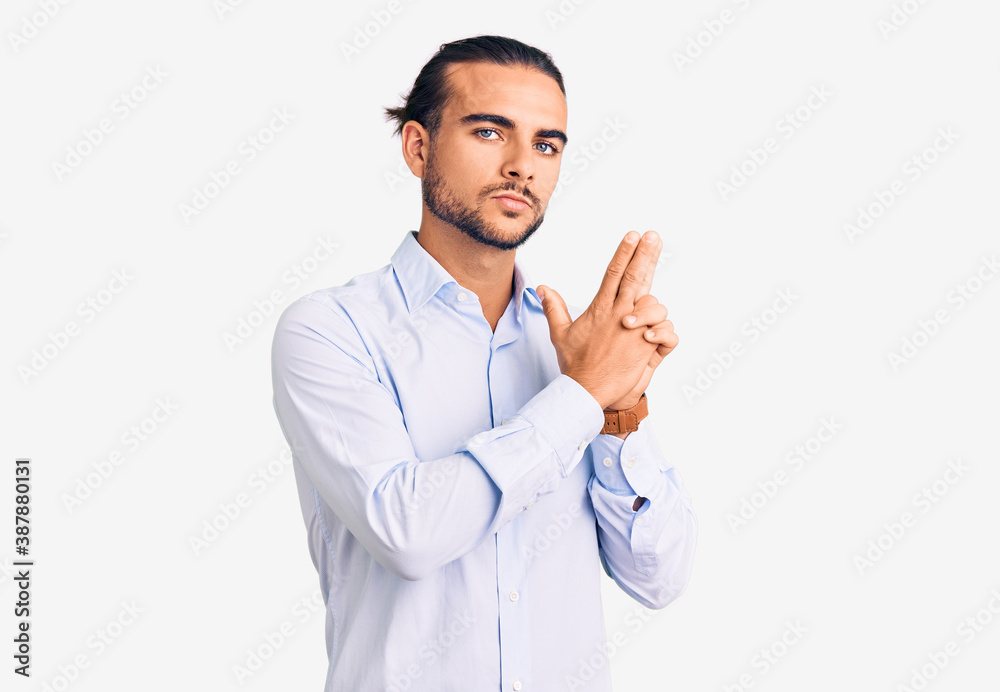 Young handsome man wearing business clothes holding symbolic gun with hand gesture, playing killing shooting weapons, angry face Young handsome man wearing business clothes holding symbolic gun with hand gesture, playing killing shooting weapons, angry face