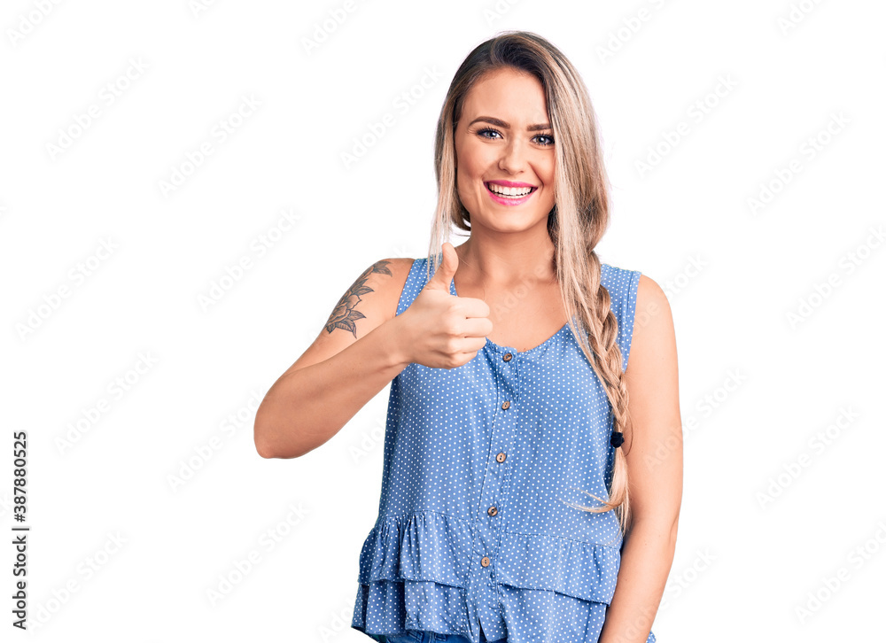 Young beautiful blonde woman wearing casual sleeveless t-shirt smiling happy and positive, thumb up doing excellent and approval sign Young beautiful blonde woman wearing casual sleeveless t-shirt smiling happy and positive, thumb up doing excellent and approval sign