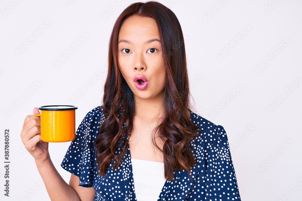 Young beautiful chinese girl holding coffee scared and amazed with open mouth for surprise, disbelief face Young beautiful chinese girl holding coffee scared and amazed with open mouth for surprise, disbelief face