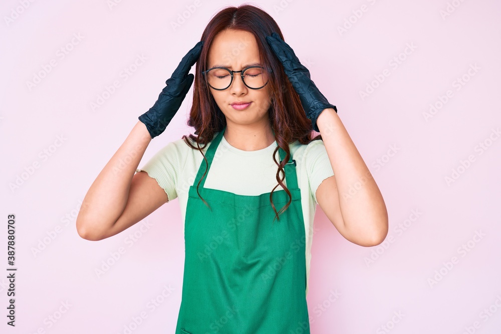 Young beautiful chinese girl wearing cleaner apron with hand on head for pain in head because stress. suffering migraine.