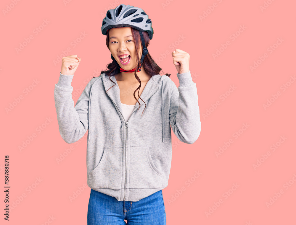 Young beautiful chinese girl wearing bike helmet screaming proud, celebrating victory and success very excited with raised arms Young beautiful chinese girl wearing bike helmet screaming proud, celebrating victory and success very excited with raised arms