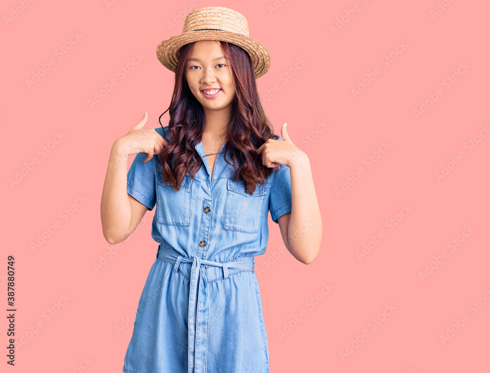 Young beautiful chinese girl wearing summer hat looking confident with smile on face, pointing oneself with fingers proud and happy. Young beautiful chinese girl wearing summer hat looking confident with smile on face, pointing oneself with fingers proud and happy.