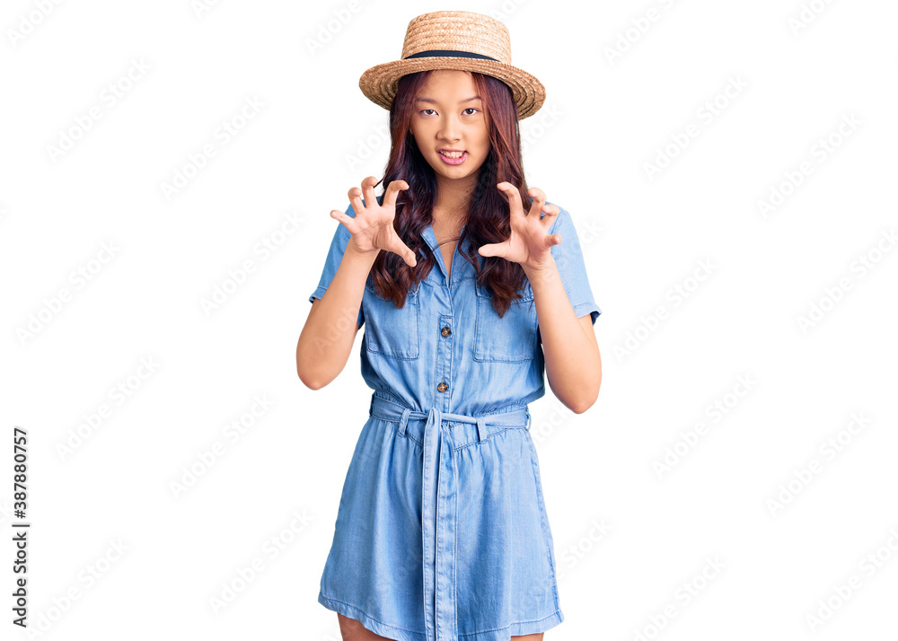 Young beautiful chinese girl wearing summer hat smiling funny doing claw gesture as cat, aggressive and sexy expression Young beautiful chinese girl wearing summer hat smiling funny doing claw gesture as cat, aggressive and sexy expression