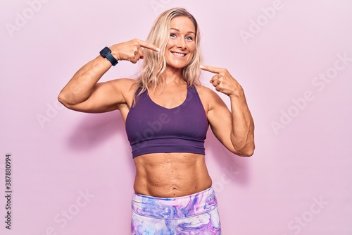 Middle age caucasian blonde woman wearing sportswear over pink background smiling cheerful showing and pointing with fingers teeth and mouth. dental health concept. © Krakenimages.com