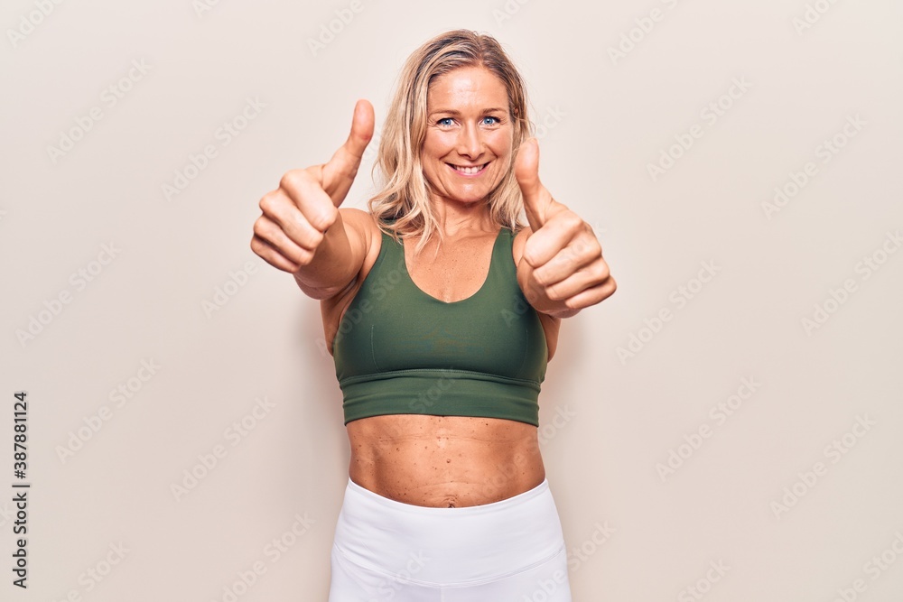 Middle age caucasian blonde woman wearing sportswear approving doing positive gesture with hand, thumbs up smiling and happy for success. winner gesture. Middle age caucasian blonde woman wearing sportswear approving doing positive gesture with hand, thumbs up smiling and happy for success. winner gesture.