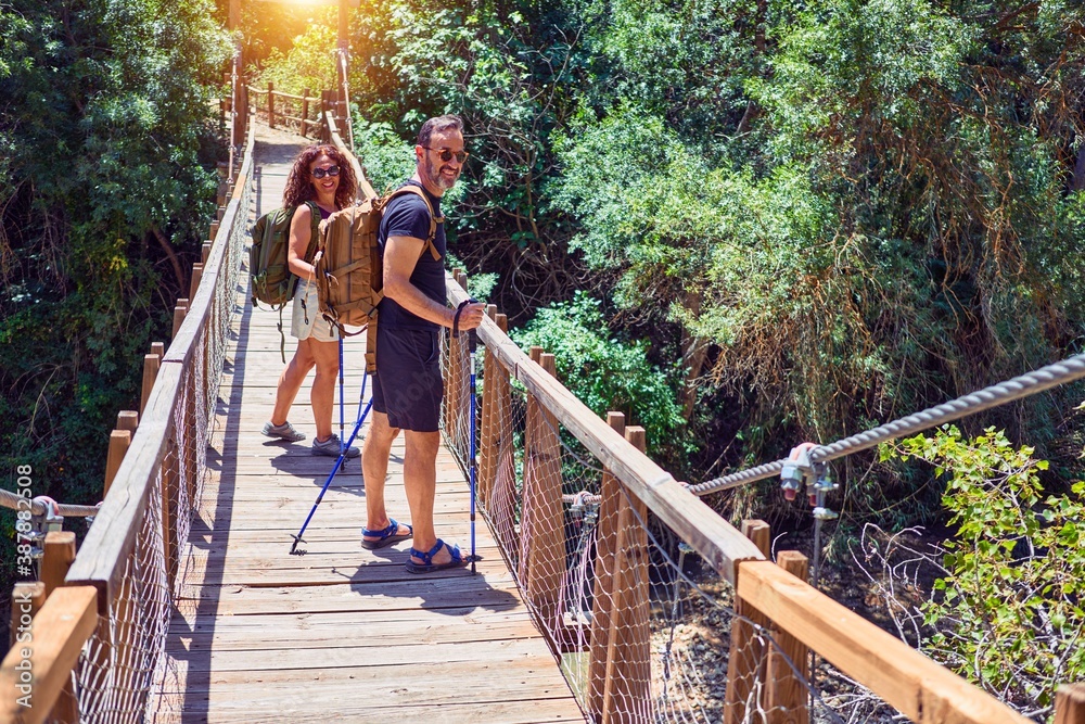 Beautiful couple of hiker wearing explorer clothes and backpack smiling happy. Standing with smile on face at runway over forest landscape background Beautiful couple of hiker wearing explorer clothes and backpack smiling happy. Standing with smile on face at runway over forest landscape background