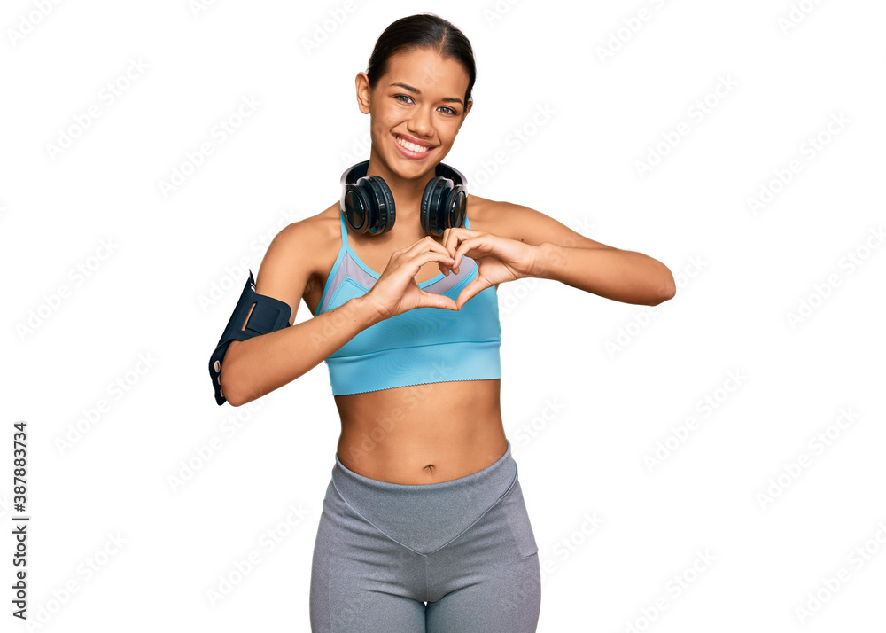 Beautiful hispanic woman wearing sportswear and headphones smiling in love showing heart symbol and shape with hands. romantic concept. Beautiful hispanic woman wearing sportswear and headphones smiling in love showing heart symbol and shape with hands. romantic concept.