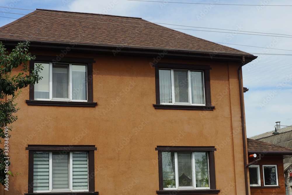 facade of a large private brown house with tiled roof windows against a blue sky