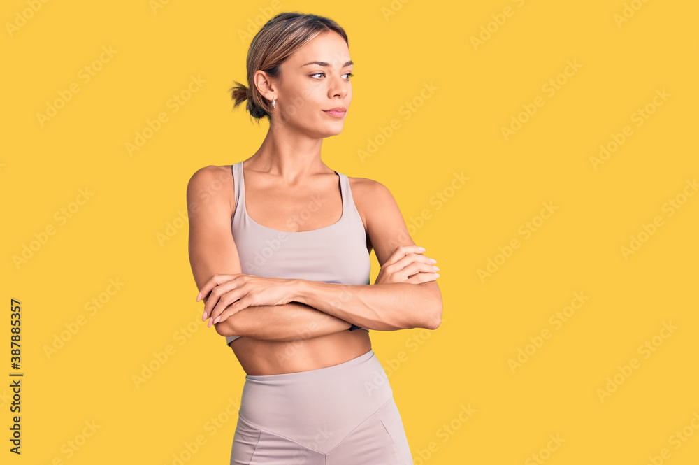 Beautiful caucasian woman wearing sportswear looking to the side with arms crossed convinced and confident Beautiful caucasian woman wearing sportswear looking to the side with arms crossed convinced and confident