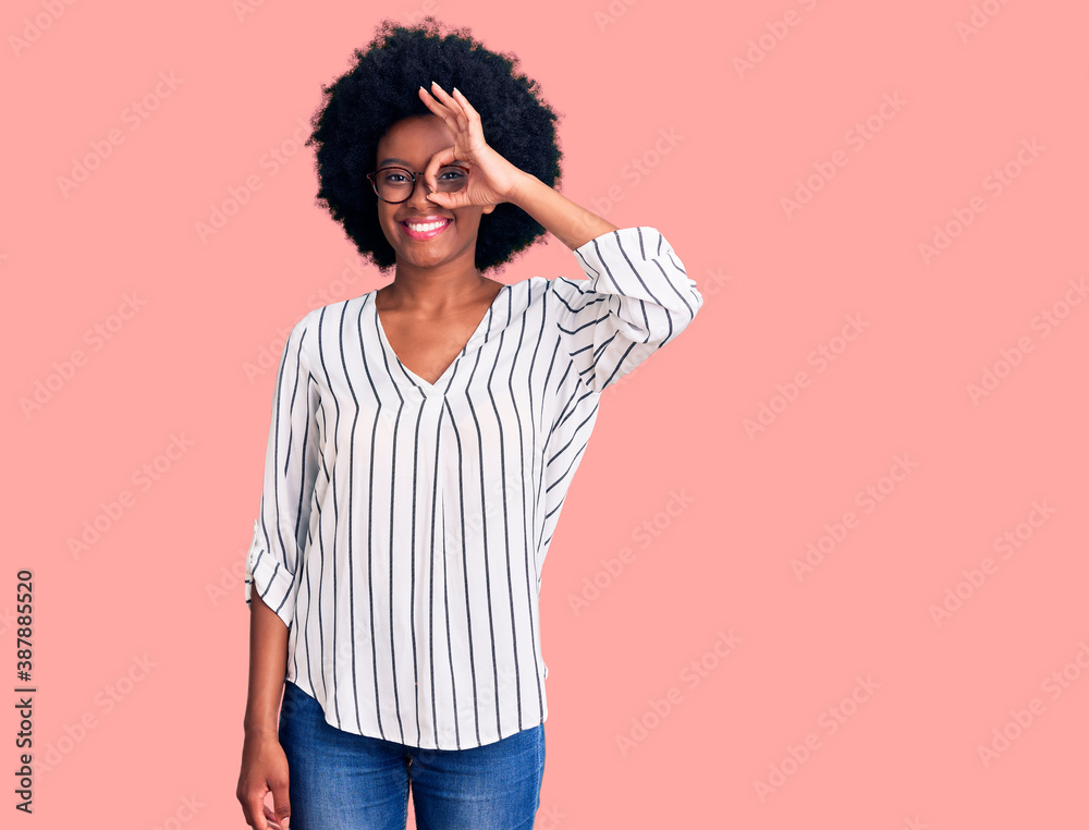 Young african american woman wearing casual clothes and glasses doing ok gesture with hand smiling, eye looking through fingers with happy face. Young african american woman wearing casual clothes and glasses doing ok gesture with hand smiling, eye looking through fingers with happy face.
