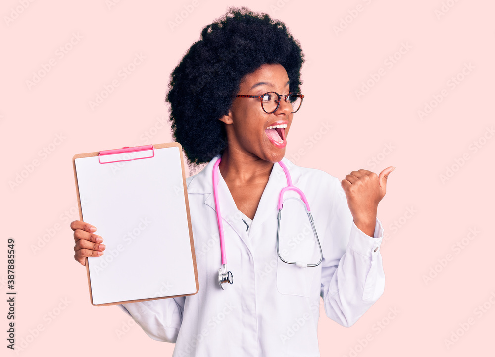 Young african american woman wearing doctor stethoscope holding clipboard pointing thumb up to the side smiling happy with open mouth