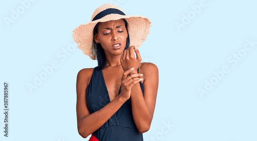 Young african american woman wearing swimsuit and summer hat suffering pain on hands and fingers, arthritis inflammation © Krakenimages.com