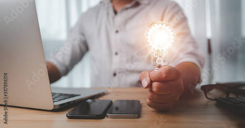 Foto Male hand holding a light bulb And there is a gear icon in it And he is using a notebook computer