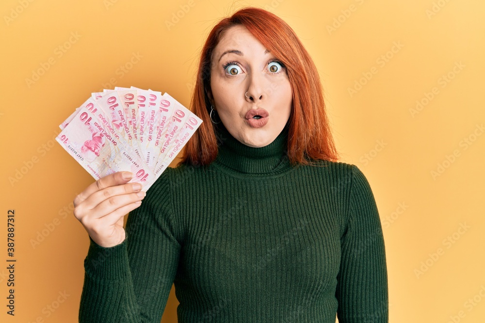 Beautiful redhead woman holding 10 turkish lira banknotes scared and amazed with open mouth for surprise, disbelief face Beautiful redhead woman holding 10 turkish lira banknotes scared and amazed with open mouth for surprise, disbelief face