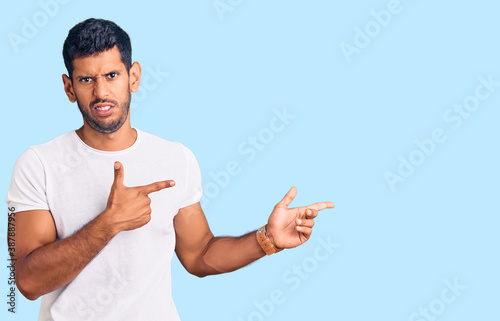 Young latin man wearing casual clothes pointing aside worried and nervous with both hands, concerned and surprised expression