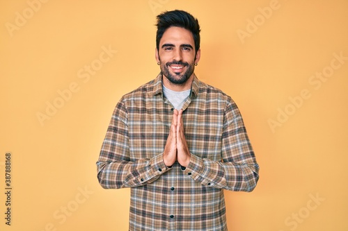 Handsome hispanic man with beard wearing casual clothes praying with hands together asking for forgiveness smiling confident.