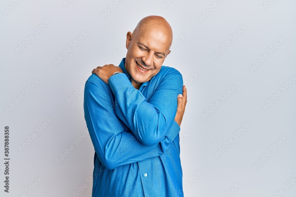 Middle age bald man wearing casual clothes hugging oneself happy and positive, smiling confident. self love and self care Middle age bald man wearing casual clothes hugging oneself happy and positive, smiling confident. self love and self care