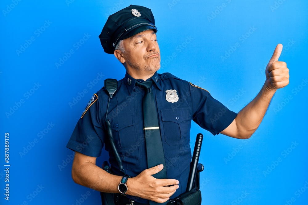Handsome middle age mature man wearing police uniform looking proud, smiling doing thumbs up gesture to the side Handsome middle age mature man wearing police uniform looking proud, smiling doing thumbs up gesture to the side