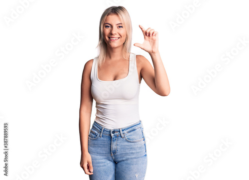 Young beautiful blonde woman wearing casual sleeveless t-shirt smiling and confident gesturing with hand doing small size sign with fingers looking and the camera. measure concept.