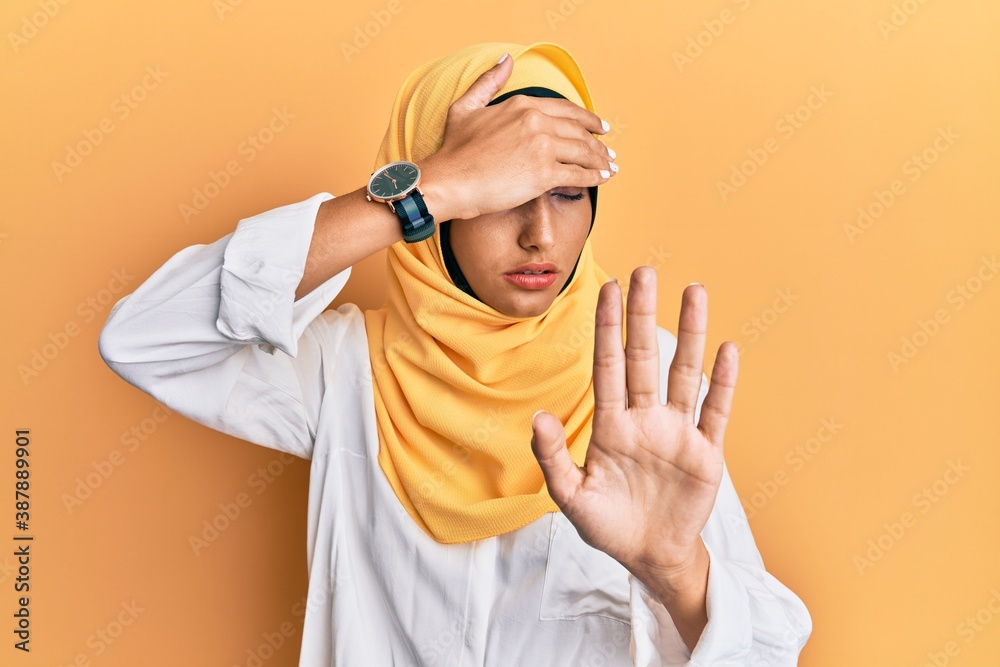 Young brunette arab woman wearing traditional islamic hijab scarf covering eyes with hands and doing stop gesture with sad and fear expression. embarrassed and negative concept. Young brunette arab woman wearing traditional islamic hijab scarf covering eyes with hands and doing stop gesture with sad and fear expression. embarrassed and negative concept.