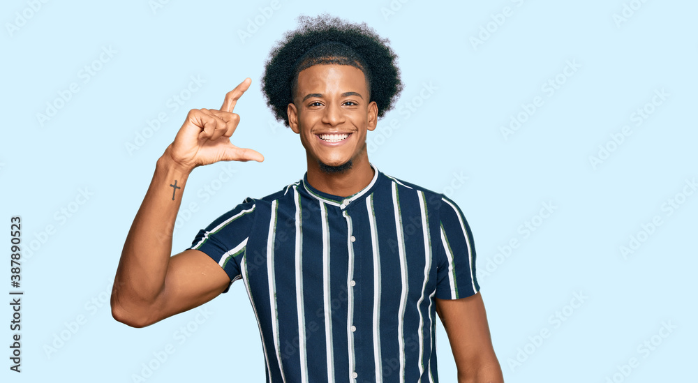 African american man with afro hair wearing casual clothes smiling and confident gesturing with hand doing small size sign with fingers looking and the camera. measure concept. African american man with afro hair wearing casual clothes smiling and confident gesturing with hand doing small size sign with fingers looking and the camera. measure concept.