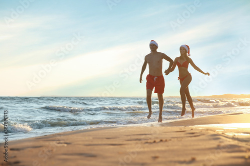 Happy couple with Santa hats together on beach. Christmas vacation