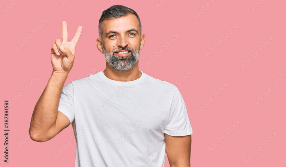 Middle age handsome man wearing casual white tshirt smiling looking to the camera showing fingers doing victory sign. number two. Middle age handsome man wearing casual white tshirt smiling looking to the camera showing fingers doing victory sign. number two.