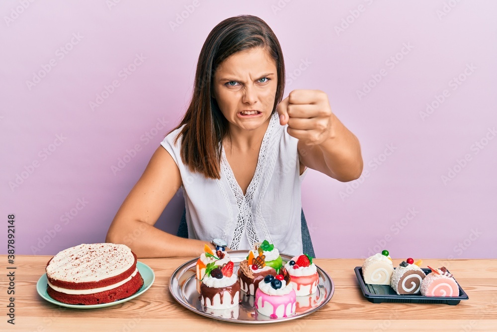 Young caucasian woman eating pastries annoyed and frustrated shouting with anger, yelling crazy with anger and hand raised Young caucasian woman eating pastries annoyed and frustrated shouting with anger, yelling crazy with anger and hand raised