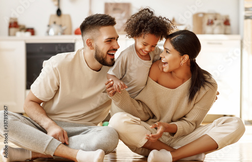 happy multiethnic family mom, dad and child  laughing, playing and tickles    on floor in cozy kitchen at home.