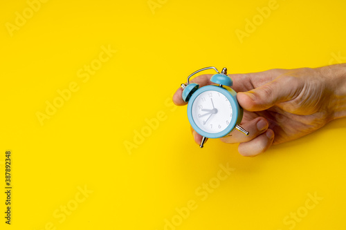 Fototapeta Naklejka Na Ścianę i Meble -  person holding old blue clock over yellow background. copy space. studio shot. time concept. schedule symbol