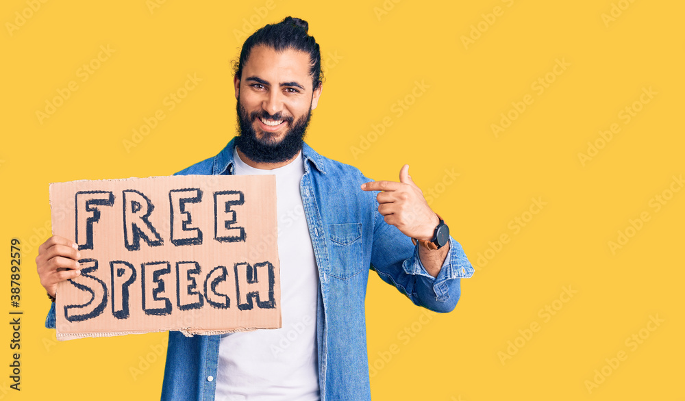 Young arab man holding free speech banner pointing finger to one self smiling happy and proud Young arab man holding free speech banner pointing finger to one self smiling happy and proud