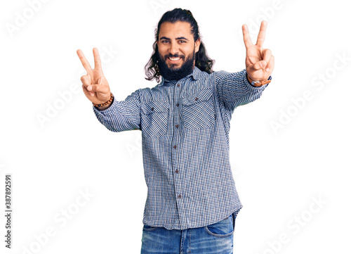 Young arab man wearing casual clothes smiling with tongue out showing fingers of both hands doing victory sign. number two.