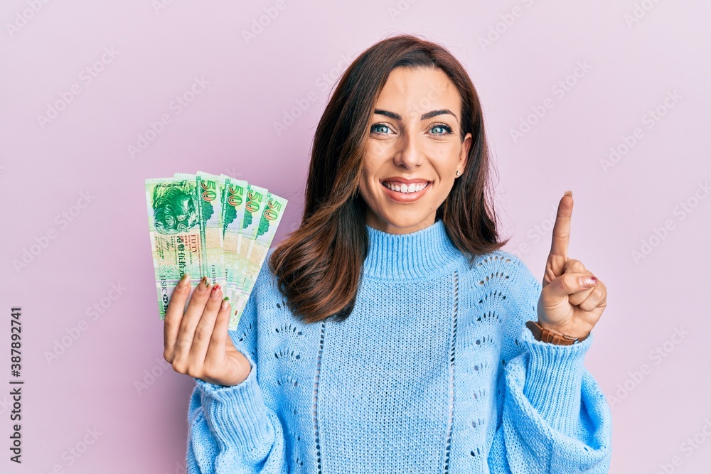 Young brunette woman holding hong kong 50 dollars banknotes smiling with an idea or question pointing finger with happy face, number one Young brunette woman holding hong kong 50 dollars banknotes smiling with an idea or question pointing finger with happy face, number one