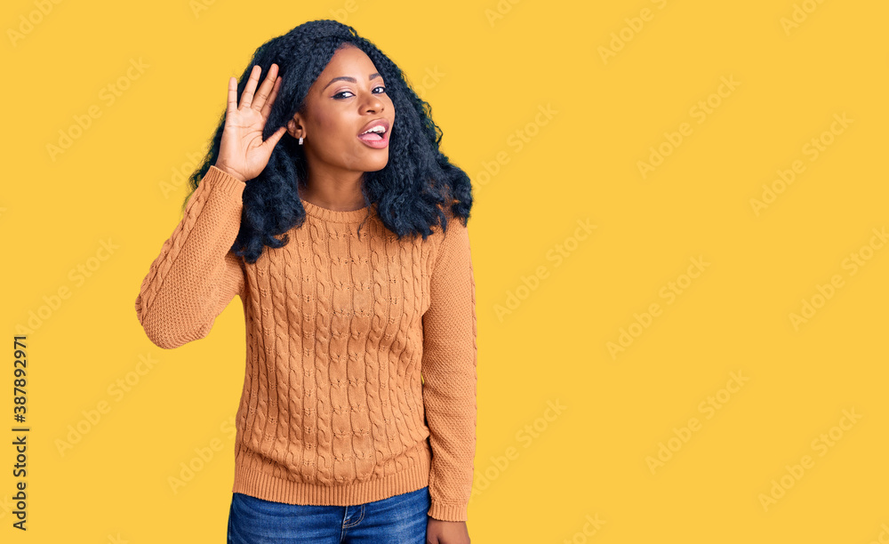 Beautiful african american woman wearing casual sweater smiling with hand over ear listening an hearing to rumor or gossip. deafness concept. Beautiful african american woman wearing casual sweater smiling with hand over ear listening an hearing to rumor or gossip. deafness concept.