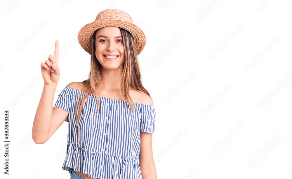 Young beautiful girl wearing hat and t shirt showing and pointing up with finger number one while smiling confident and happy. Young beautiful girl wearing hat and t shirt showing and pointing up with finger number one while smiling confident and happy.
